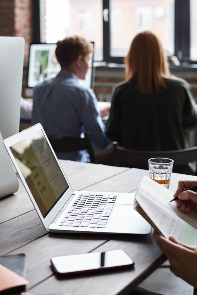 Someone working on their laptop with two people in the background