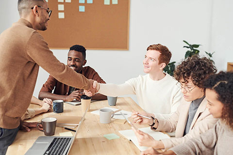 People around an office table and two of them are shaking hands